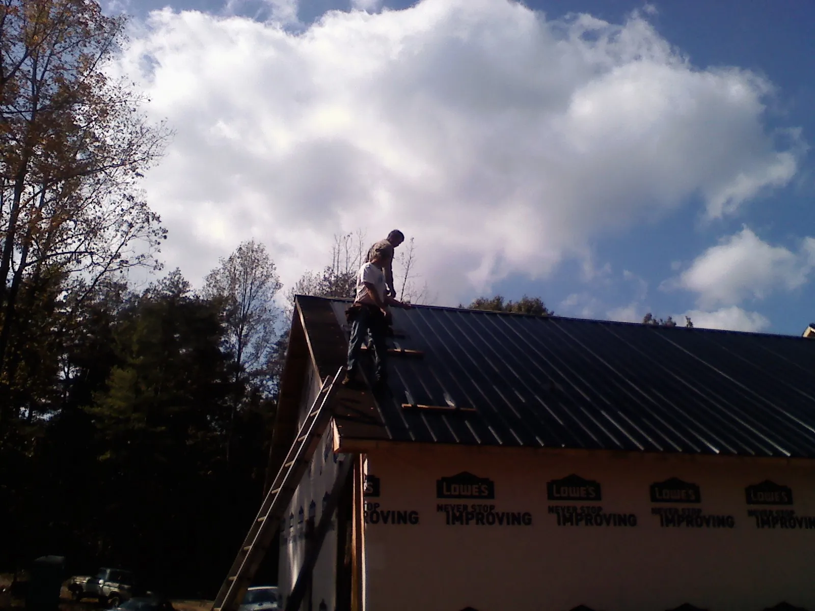 Roofer fastening dark metal panels high against a cloudy sky, from a Roof Inspection job in Lawrenceburg
