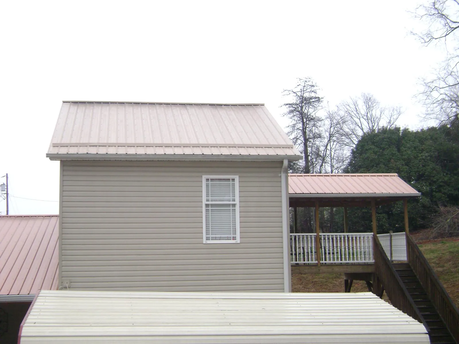 Tan metal roofs on a two story addition and attached porch, from a Roof Replacement job in Lawrenceburg